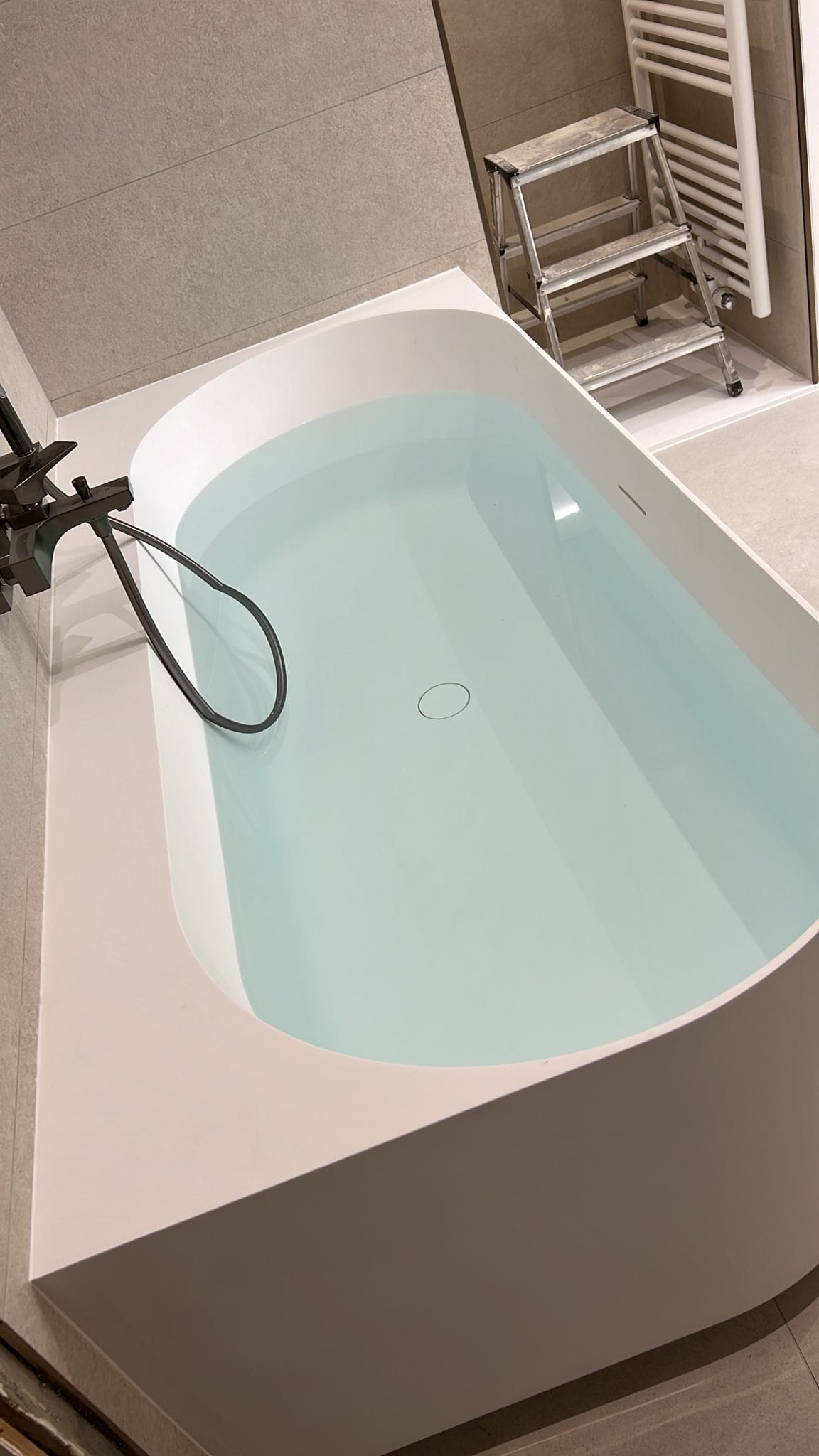 Baignoire îlot blanche avec robinetterie noire dans une salle de bain rénovée par Yce Confort